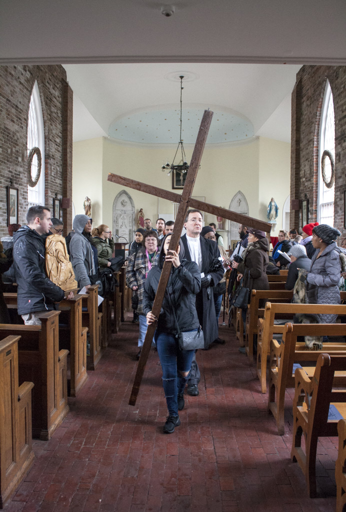 Maria Celeste Lara of St. Monica-St. Augustine Church carries the cross out of St. Augustine Cemetery Chapel, one of the stations during the outdoor ecumenical Way of the Cross on Friday, March 25, 2016, in South Boston. (Photo by Susan Doucet)