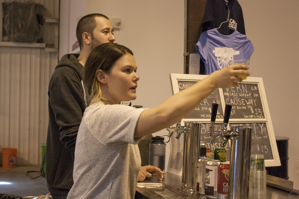 Becky Bond, a tasting and retail associate at Castle Island Brewing Company in Norwood, hands a sample of beer to a customer on Thursday, March 31, 2016. (Photo by Susan Doucet)